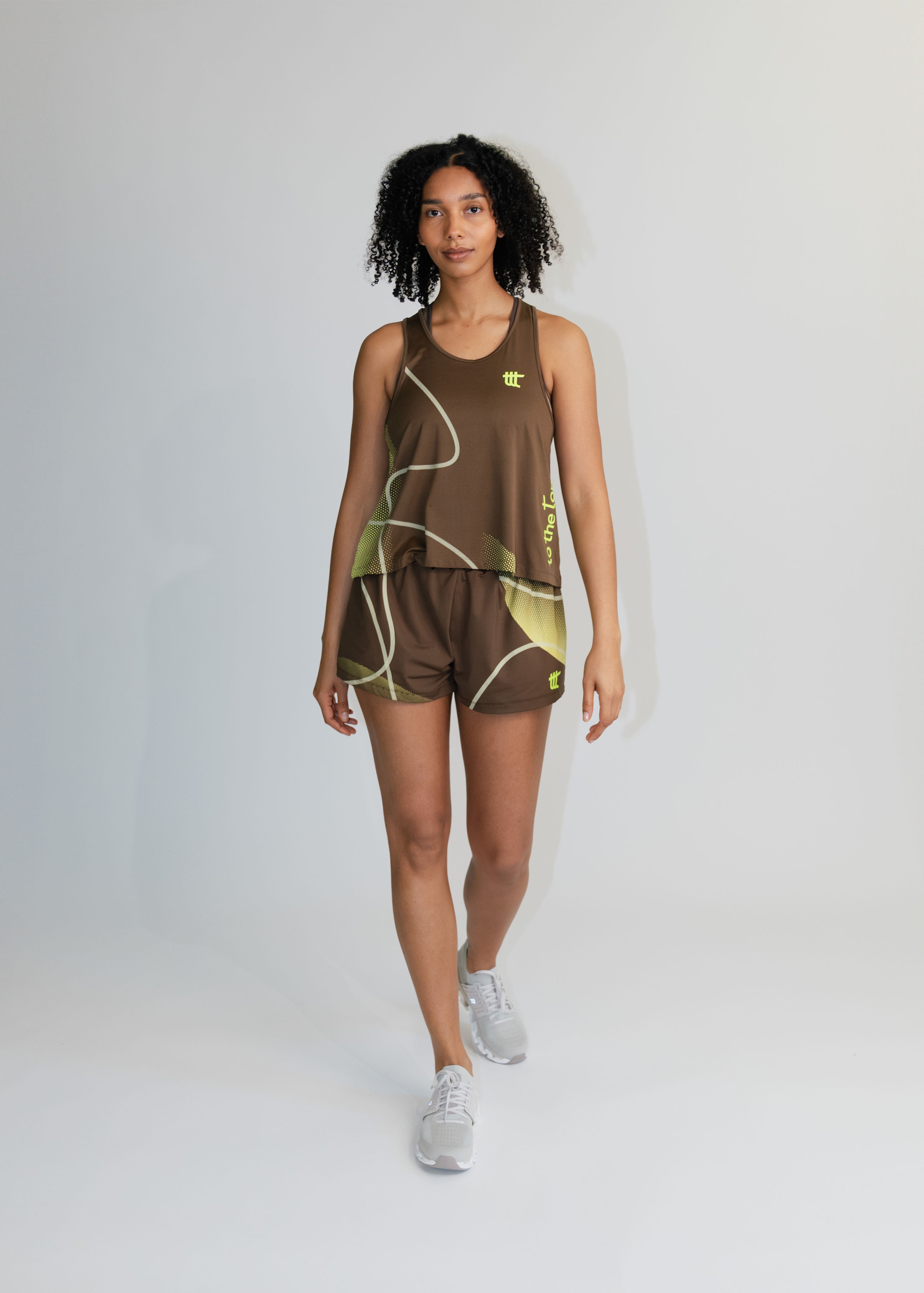 Model trägt das braune Pace Tank Top als Teil eines modischen Athleisure-Outfits