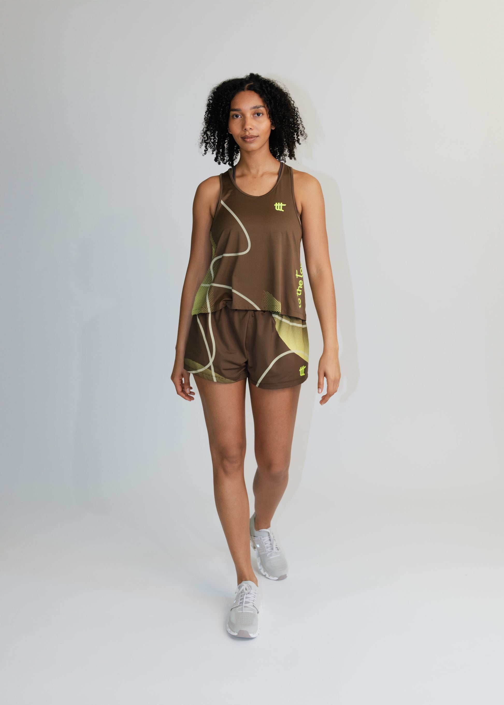 Model trägt das braune Pace Tank Top als Teil eines modischen Athleisure-Outfits